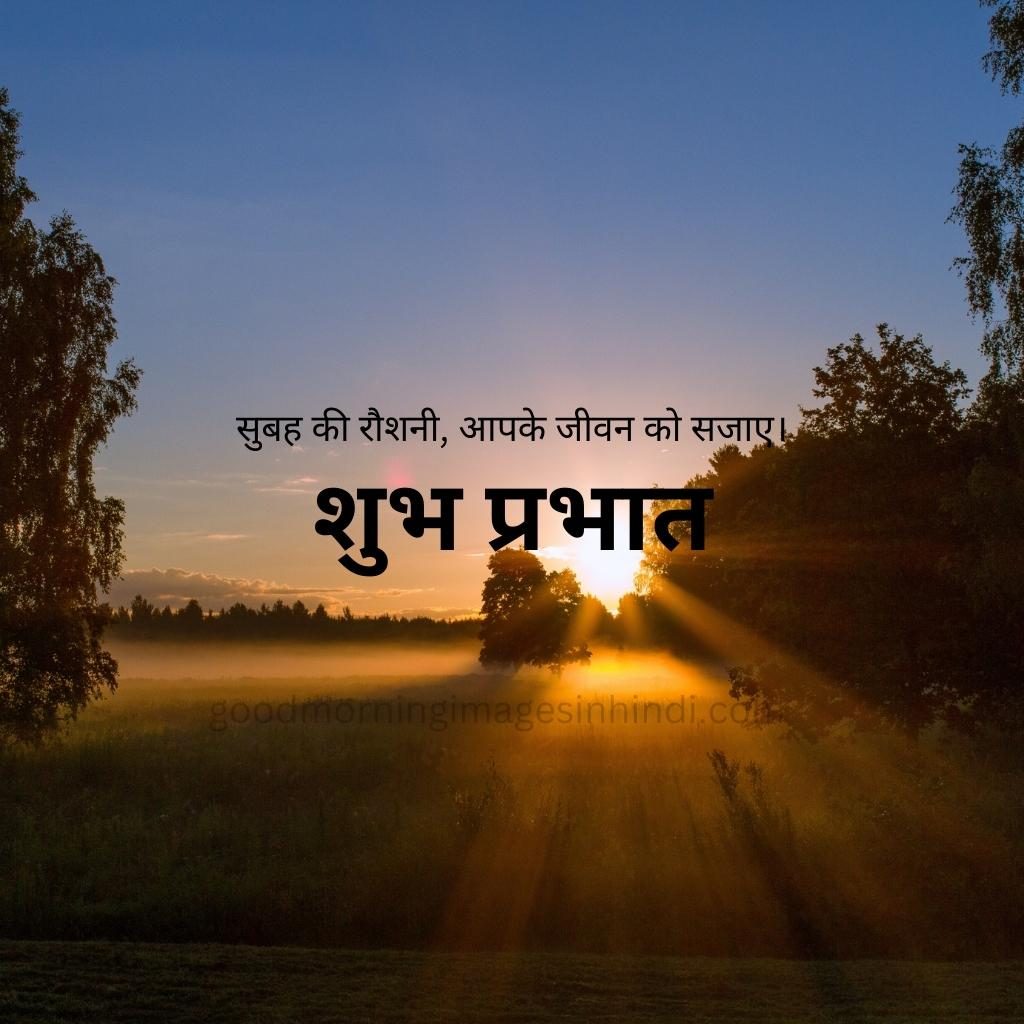 Shubh Prabhat! A single yellow sun hangs low on the horizon, silhouetted against a backdrop of snow-capped mountains and streaky clouds, trees all over good morning images in hindi